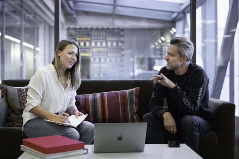 Two business professionals in a conference room using a laptop to discuss professional services automation (PSA) for improved workflow efficiency.